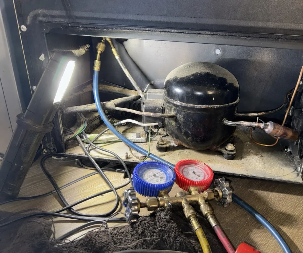 Compressor and refrigerant tubing in the lower service bay of a wine cooler with manifold gauges connected