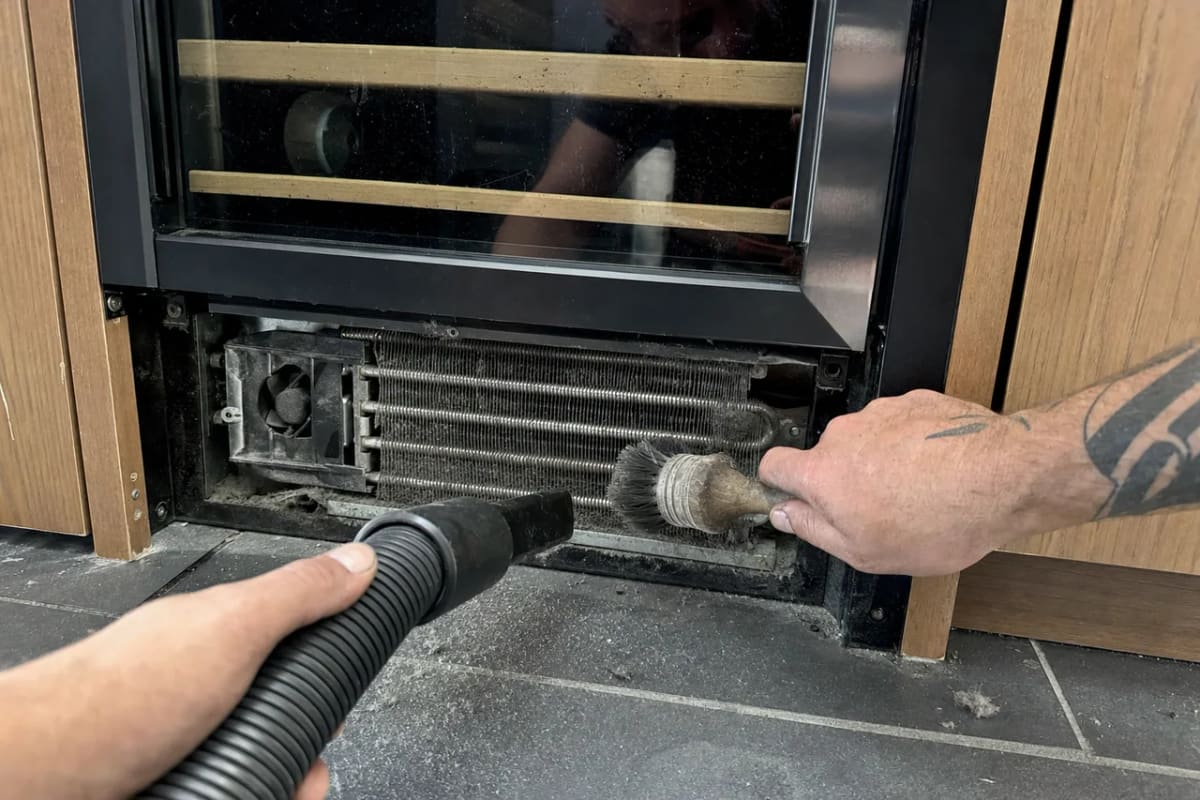 Brush and vacuum clearing dust from the condenser coil of a built-in wine cooler