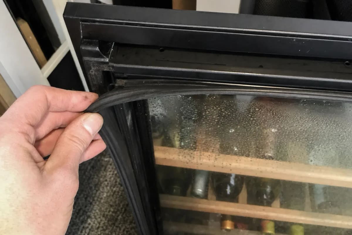 Hand pulling the magnetic door gasket away from the frame, condensation across the glass behind it