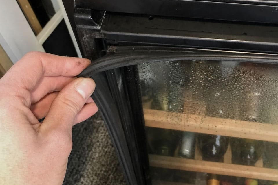 Hand pulling the magnetic door gasket clear of the frame, with condensation across the glass