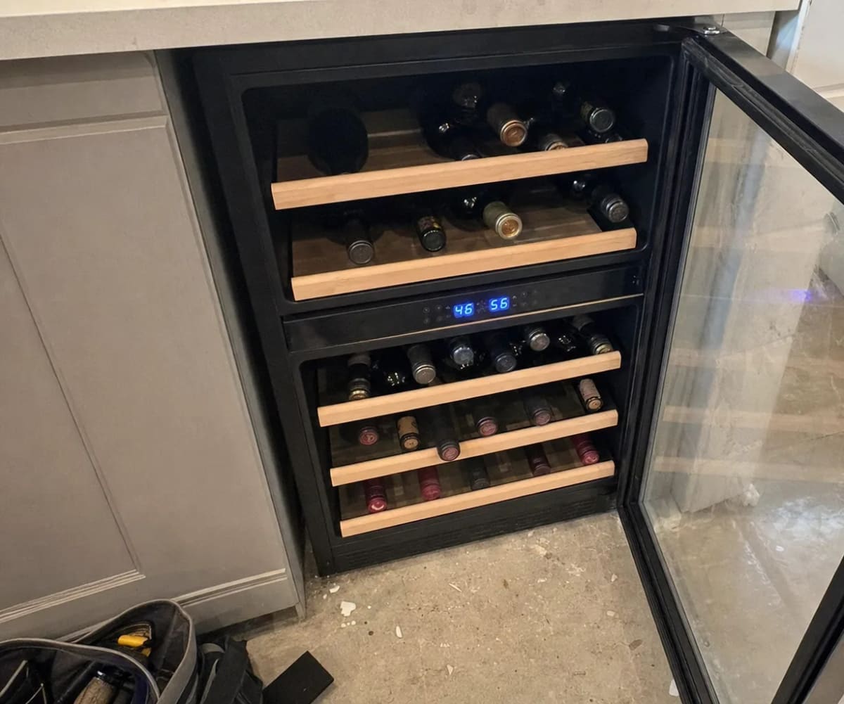 Open wine cooler with bottles on wooden shelves and a lit temperature display between two zones