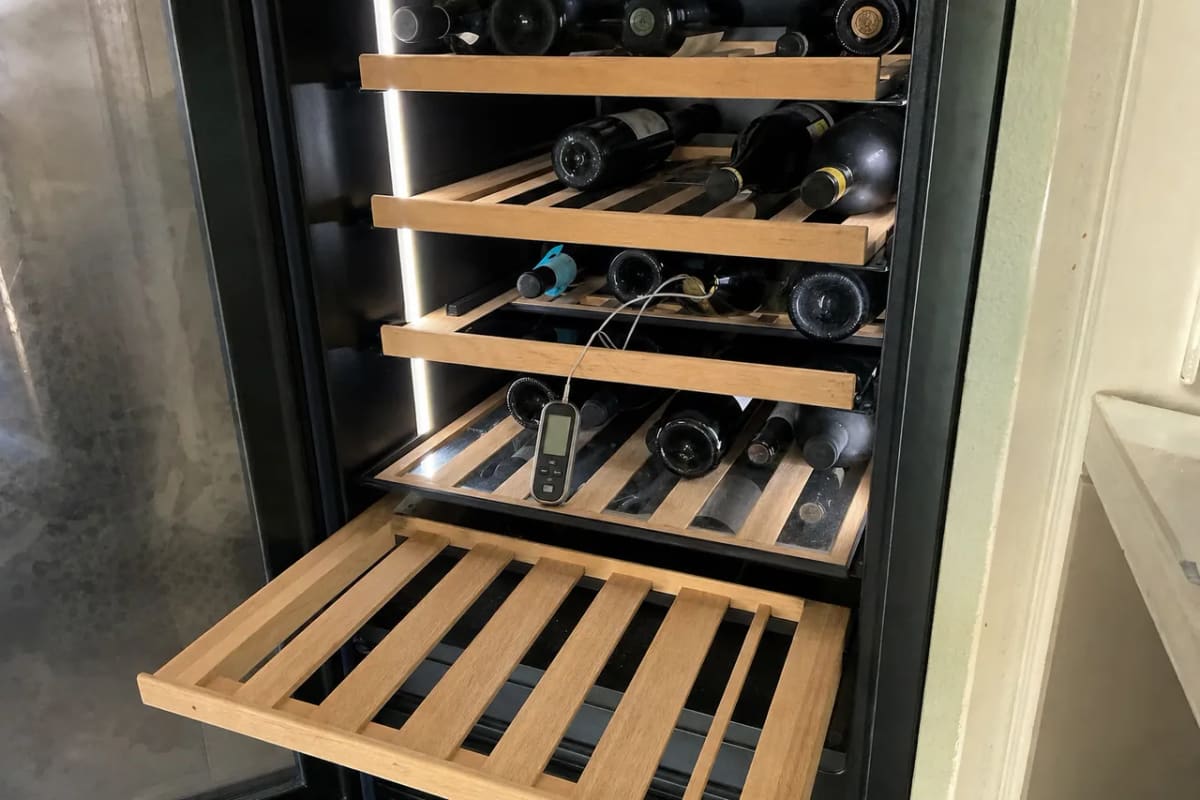 Pull-out shelves with bottles stacked to the rear cabinet wall and a probe thermometer among them
