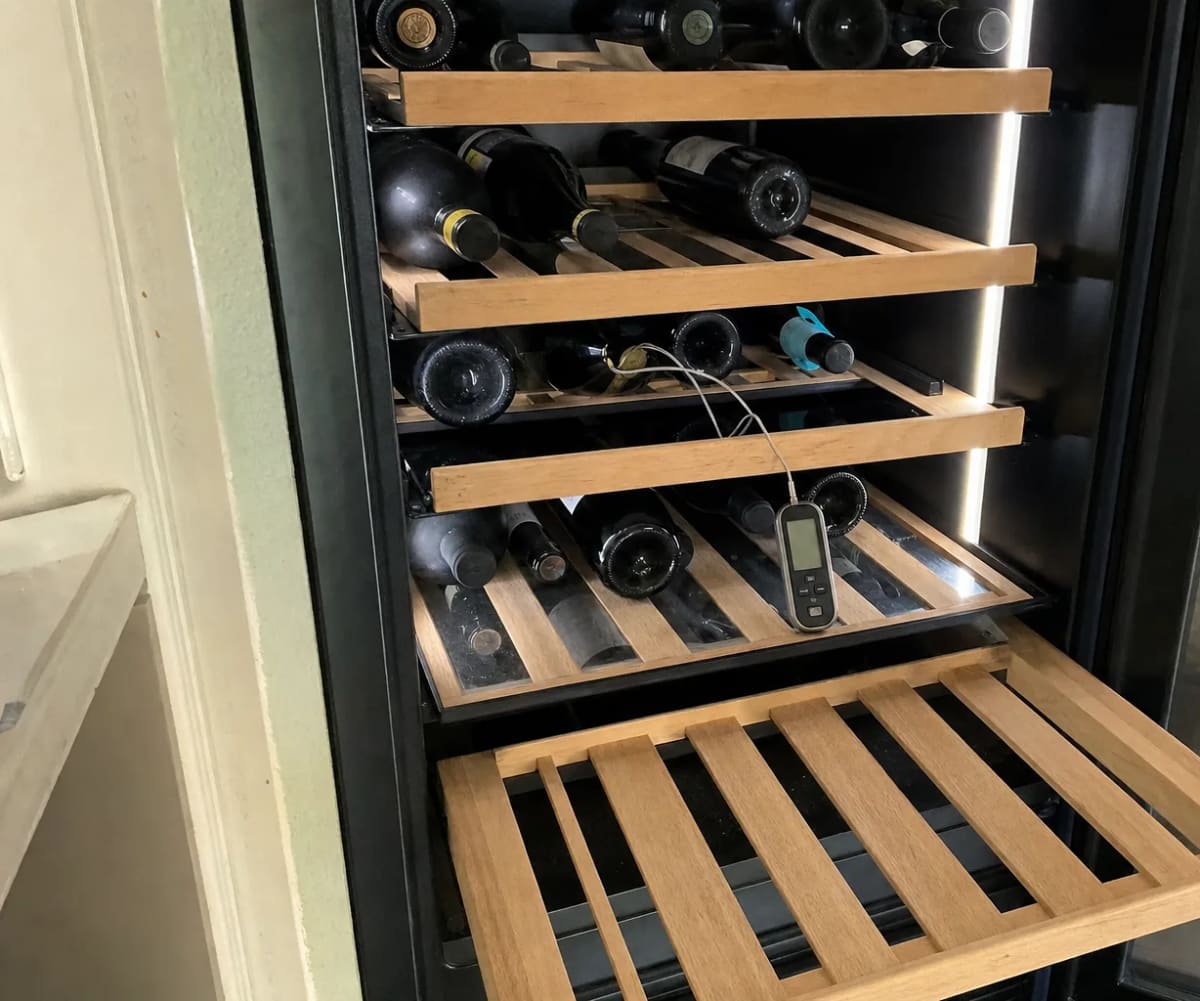 Bottles on wooden pull-out shelves with a probe thermometer left on the middle shelf