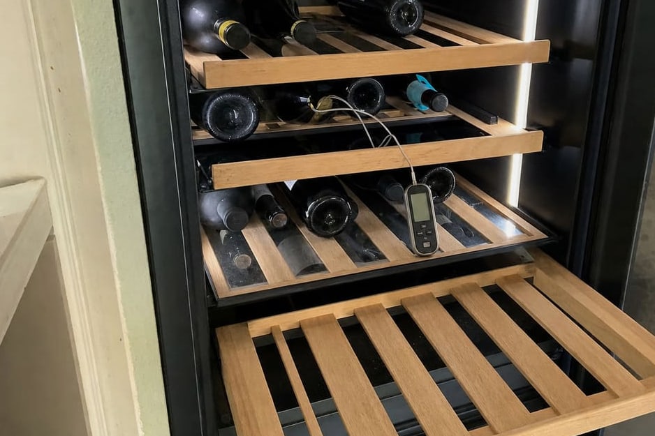 Wooden shelf pulled out of a wine cooler, bottles on their sides and a probe thermometer on the shelf