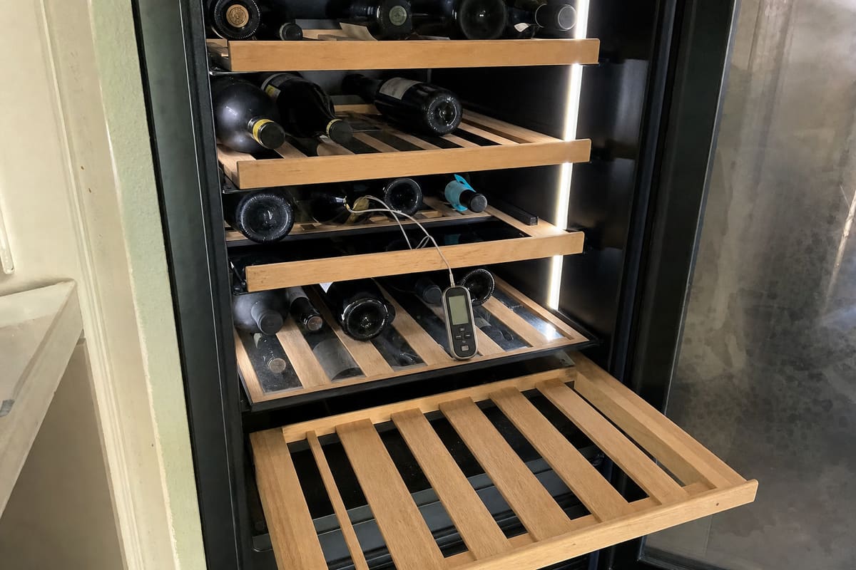 Wooden pull-out shelves loaded with bottles, a probe thermometer resting on the middle shelf