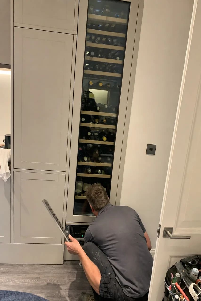 Full-height wine column loaded with bottles, built into a cabinet run, with a technician at its base