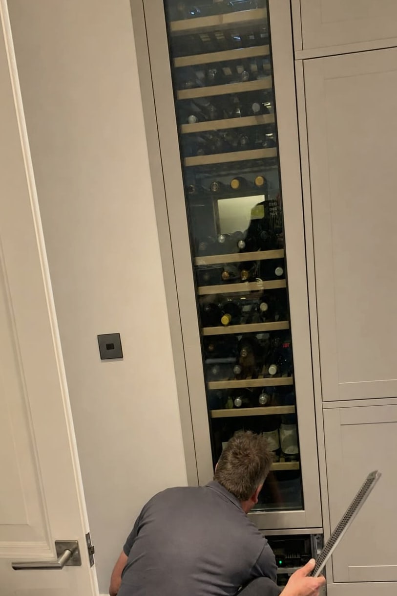 Full-height built-in wine column filled with bottles, a technician working at the base of the cabinet run