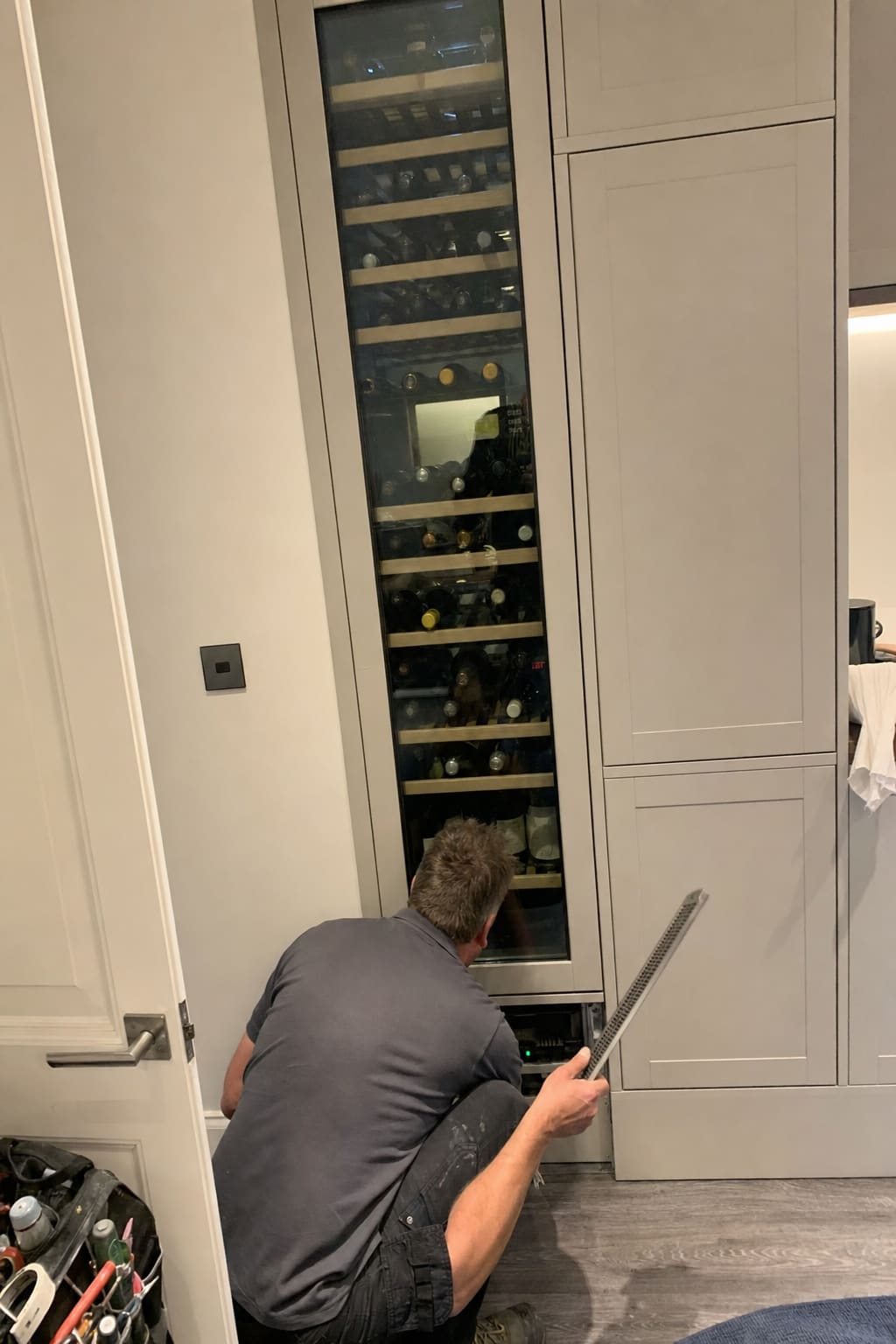 Full-height wine column built flush into kitchen cabinetry, technician working at the base