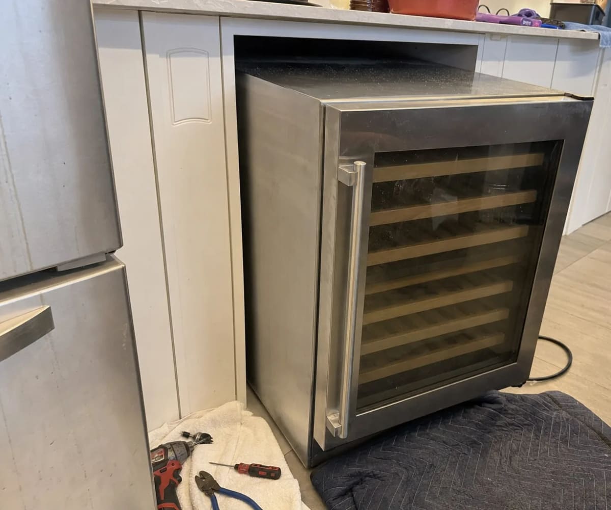 Wine cooler drawn out of its kitchen cabinet opening with tools on the floor beside it