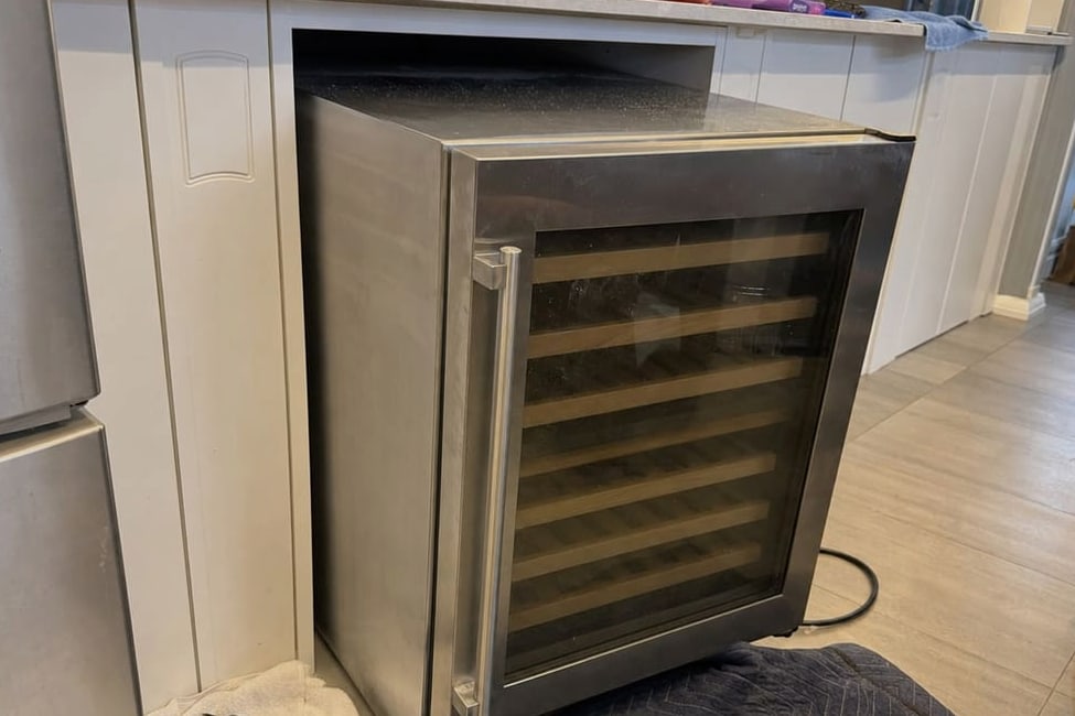 Under-counter wine cooler pulled out of its opening, the empty cabinet void behind it